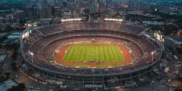 Aerial view of a major sports stadium illuminated at night during an event, surrounded by city lights.