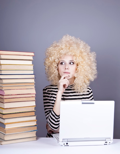 A person sitting at a desk, using a laptop, surrounded by books and college brochures, with a determined expression. The laptop screen displays a career assessment tool.