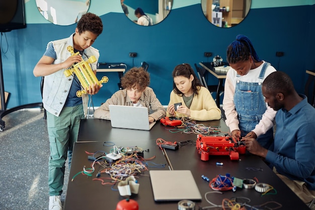 A diverse group of high school students working together on a robotics project in a vibrant makerspace. They are programming a robot, surrounded by tools and electronic components, showcasing collaborative problem-solving.