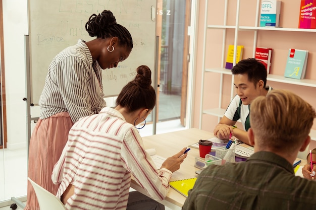 A classroom setting with a diverse group of students working on different activities. One student is using a tablet with assistive technology, another is receiving one-on-one instruction from the teacher, and others are collaborating on a group project. The caption reads, 