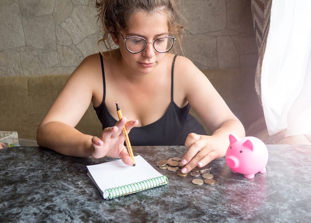 A person using a calculator and reviewing bills on a table, with coins and a piggy bank nearby, suggesting careful financial planning and debt management.