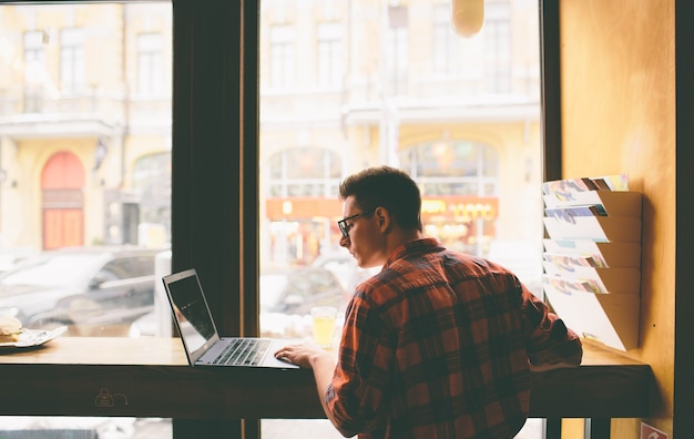 An individual working on a laptop at a coffee shop, symbolizing freelancing and supplemental income, combined with graphics representing passive income streams like stocks and rental properties.