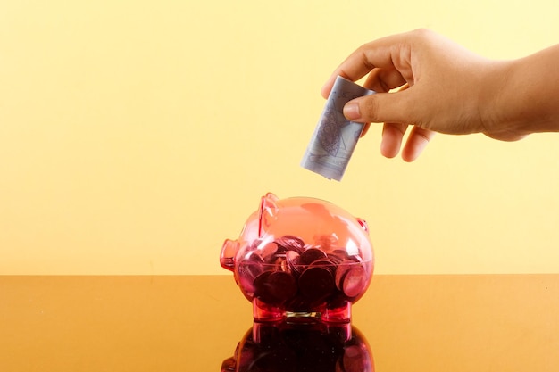 A person's hand inserting coins into a piggy bank, symbolizing saving money for a down payment.
