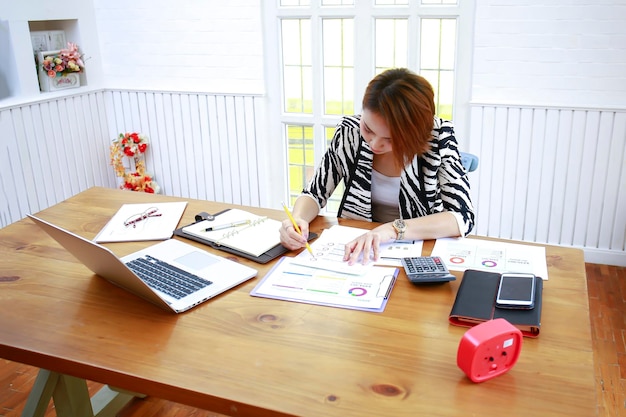 A person sitting at a desk using a budget planning app on their laptop, with a calculator and various financial documents scattered around the desk.