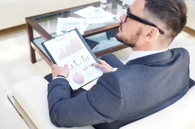 A person using a tablet to review their investment portfolio, with charts and financial data visible on the screen. The setting is a modern home office, conveying financial comfort and strategic planning.