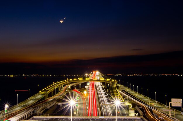 A high-speed train speeding across a newly constructed bridge, with solar panels lining the side of the tracks, representing the intersection of transportation infrastructure and sustainable energy solutions.
