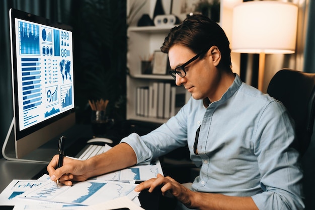 A person wearing glasses intently studying a computer screen displaying stock charts and financial data. The scene is lit by the screen, highlighting the focus and intensity of the analysis being conducted.