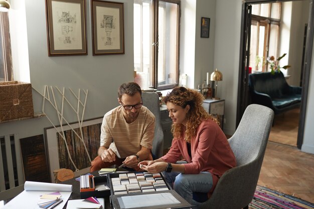 Two people sitting at a table in a well-lit, modern home office discussing financial planning. One person is pointing at a tablet displaying a savings calculator tool with fields for 401(k) contributions, IRA contributions, and projected returns. The calculator highlights the potential tax savings.