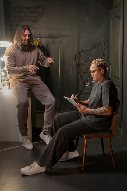 A medium shot of a director talking to two actors on set. The atmosphere is relaxed and collaborative. The director is gesturing while explaining something, and the actors are listening attentively.