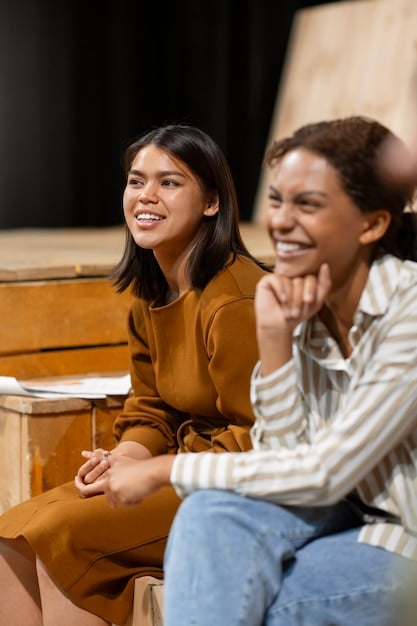 Two young actors are collaborating on a scene during a workshop. They are laughing and appear to be genuinely enjoying the process. The atmosphere is relaxed and supportive.