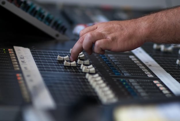 A close-up shot of a professional sound engineer adjusting levels on a mixing console in a professional audio post-production studio. The console is illuminated with various brightly colored indicators and sliders, emphasizing the technical precision and control required for sound mixing. The background is blurred, suggesting a focused and meticulous working environment.